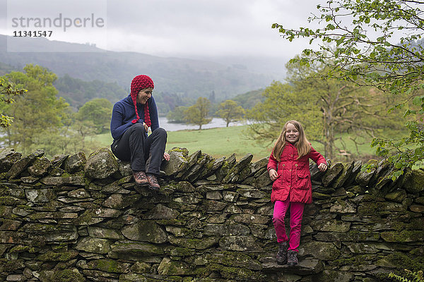 Mutter und Tochter ruhen sich im Urlaub im Lake District  Cumbria  England  Vereinigtes Königreich  Europa  auf einer Trockenmauer aus