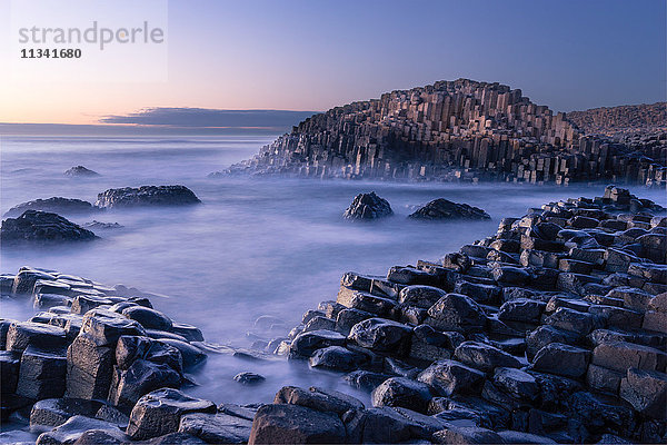 Der Giant's Causeway erhebt sich spät in der Nacht aus dem Atlantik  während das letzte Licht der Sonne hinter dem Horizont verschwindet  County Antrim  Nordirland  Vereinigtes Königreich  Europa