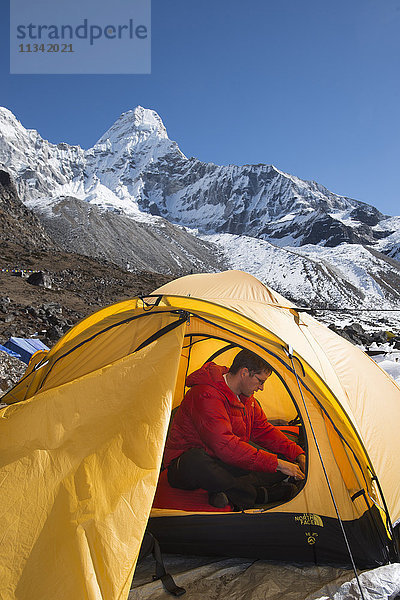 Ein Bergsteiger packt seinen Rucksack in Vorbereitung auf die Besteigung der Ama Dablam  dem 6856 m hohen Gipfel in der Ferne  Khumbu-Region  Himalaya  Nepal  Asien