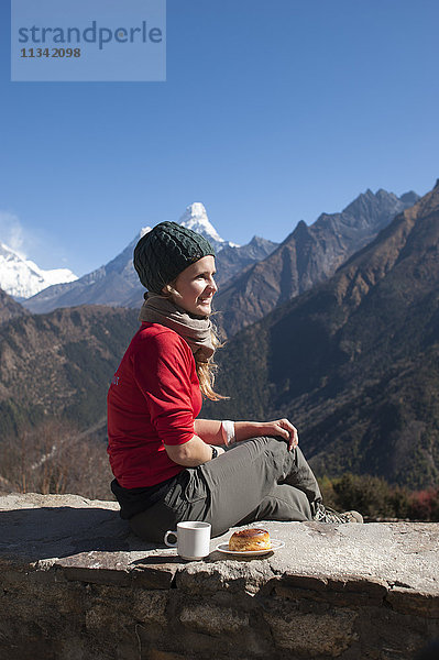 Ein Trekker macht auf dem Weg eine Pause  um zu tanken. In der Ferne ist die Ama Dablam zu sehen  Khumbu Region  Nepal  Asien