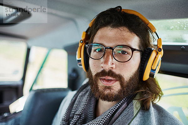 Portrait eines Mannes mit Vollbart im Auto mit Kopfhörern