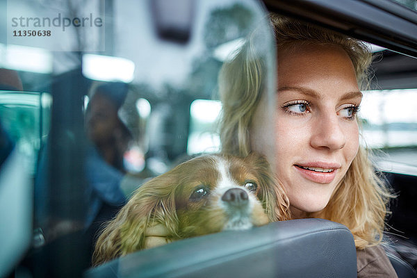Lächelnde junge Frau mit Hund im Auto schaut aus dem Fenster