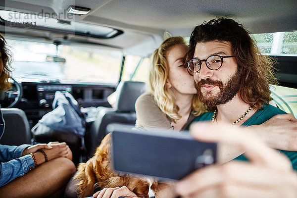 Fröhliches Paar mit Hund macht ein Selfie im Auto