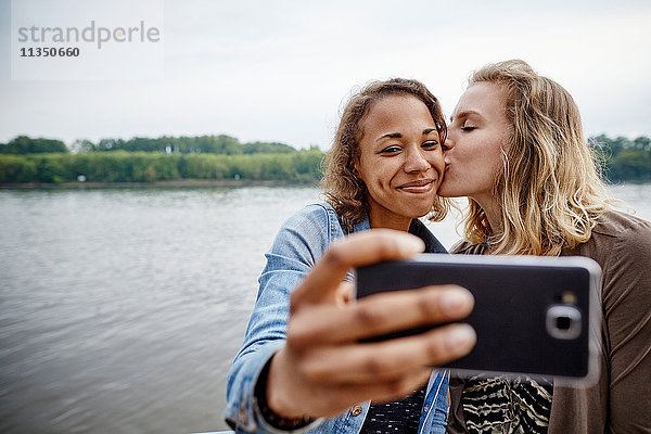 Zwei junge Frauen machen ein Selfie am Flussufer