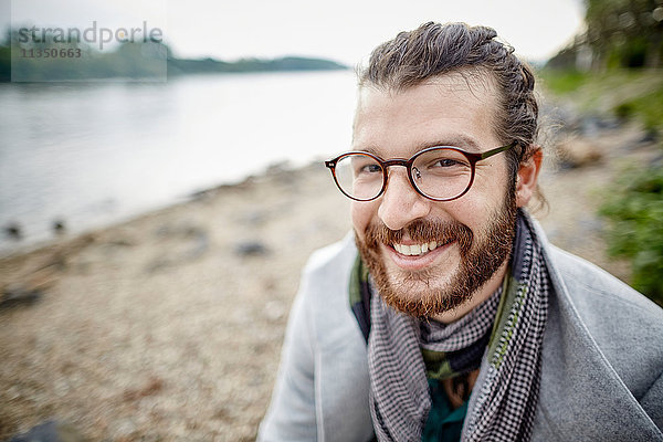 Lächelnder junger Mann mit Vollbart am Flussufer