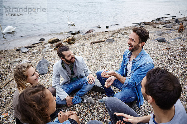 Fröhliche Freunde sitzen zusammen am Flussufer