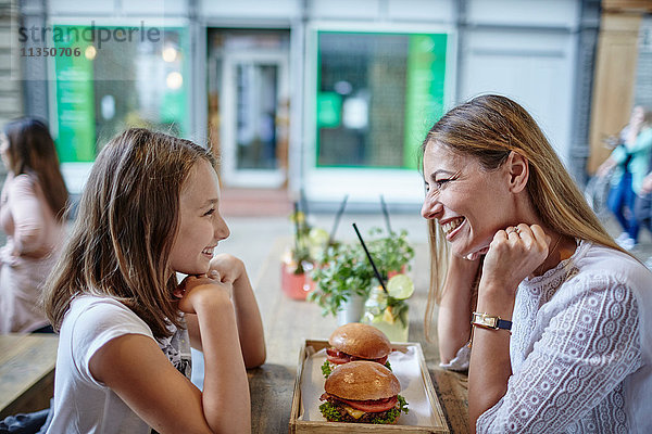 Glückliche Mutter und Tochter sitzen im Restaurant mit Hamburgern