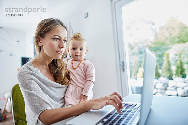 Mutter mit Baby benutzt einen Laptop Zuhause