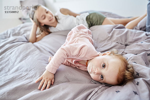 Baby liegt mit ihrer Schwester im Bett