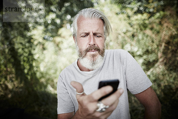 Reifer Mann mit Vollbart im Freien schaut auf Handy