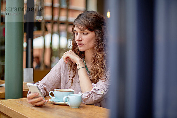 Junge Frau in einem Cafe schaut auf ihr Handy