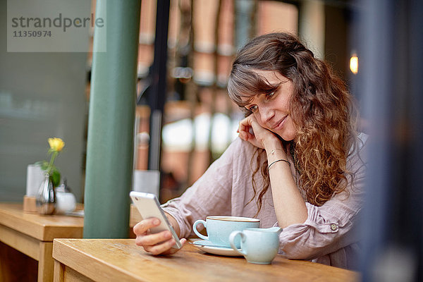 Junge Frau in einem Cafe schaut auf ihr Handy