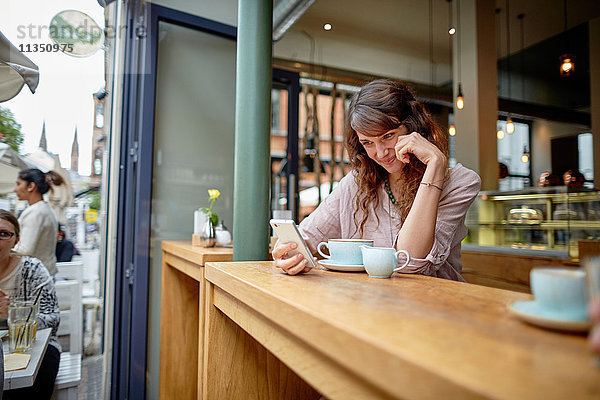 Lächelnde junge Frau in einem Cafe schaut auf ihr Handy