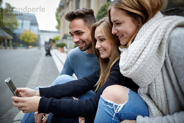 Drei lächelnde Freunde schauen zusammen auf ein Handy