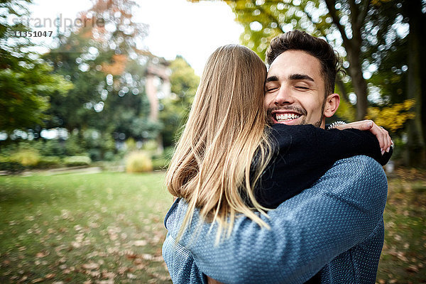 Fröhliches junges Paar umarmt sich im Park