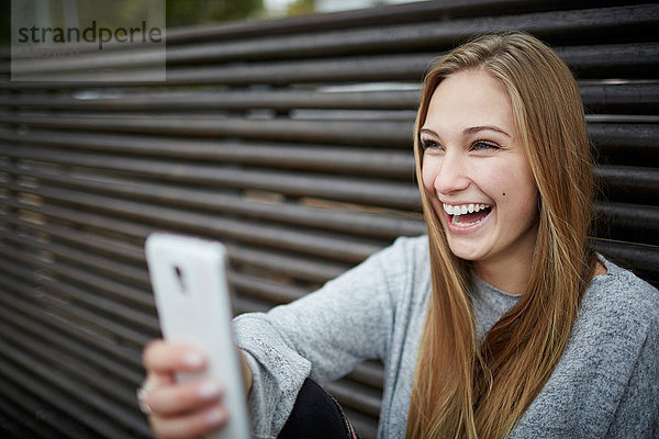 Fröhliche junge Frau mit Handy im Freien