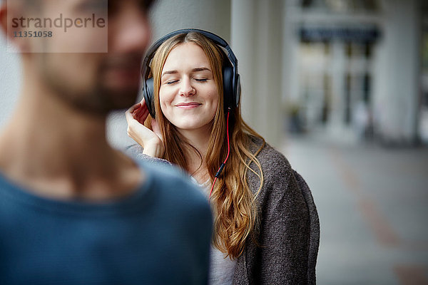 Junge Frau mit Kopfhörern im Freien und Mann im Vordergrund