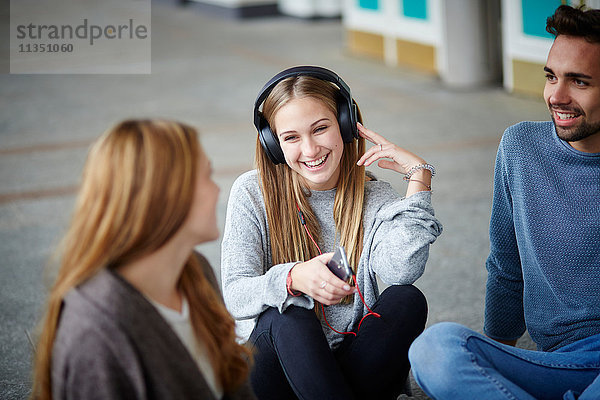Fröhliche junge Frau mit Kopfhörern sitzt mit Freunden zusammen