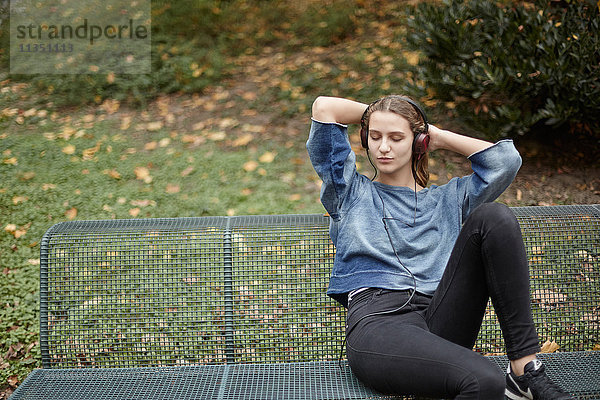 Junge Frau mit geschlossenen Augen und Kopfhörern auf einer Parkbank
