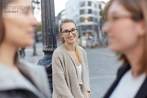 Lächelnde Frau in der Stadt mit zwei Frauen im Vordergrund