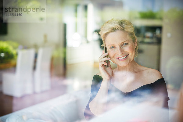 Lächelnde reife Frau telefoniert hinter Fenster