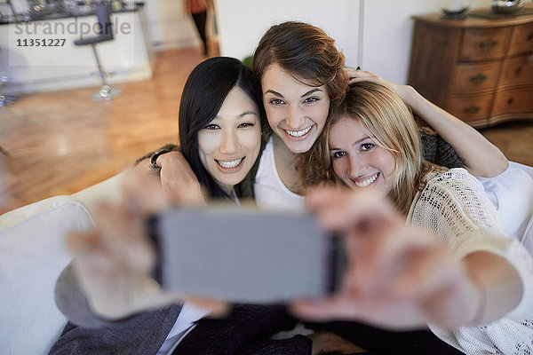 Drei fröhliche Frauen sitzen auf der Couch und machen ein Selfie