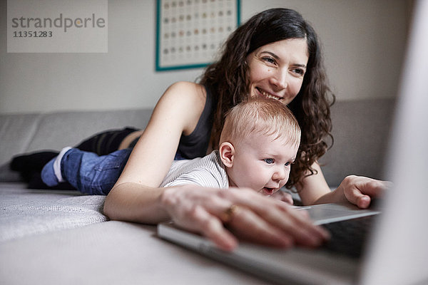 Frau mit Baby auf der Couch benutzt Laptop