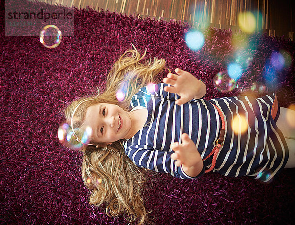 Glückliches Mädchen liegt auf einem Teppich und spielt mit Seifenblasen