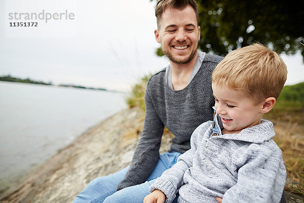 Glücklicher Vater und Sohn sitzen am Flussufer