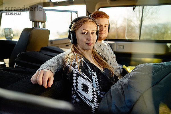 Entspanntes junges Paar mit Kopfhörern und Schlafsack in einem Auto