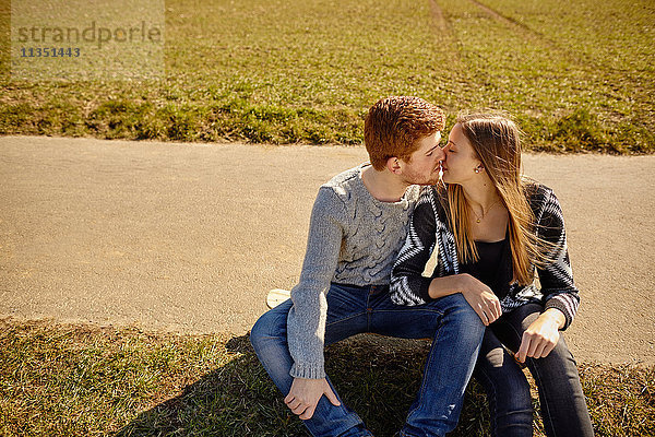 Junges Paar sitzt an einem Feldweg und küsst sich