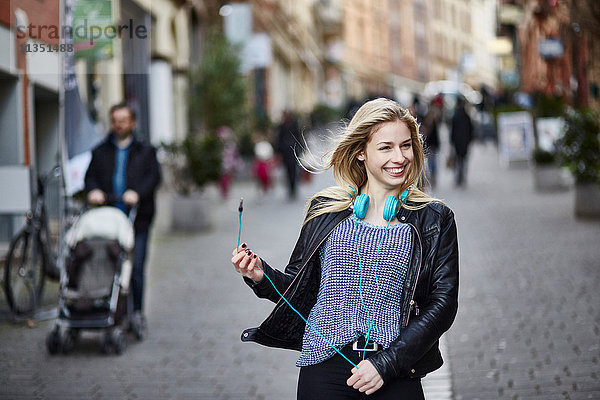 Fröhliche junge Frau mit Kopfhörern in der Fußgängerzone