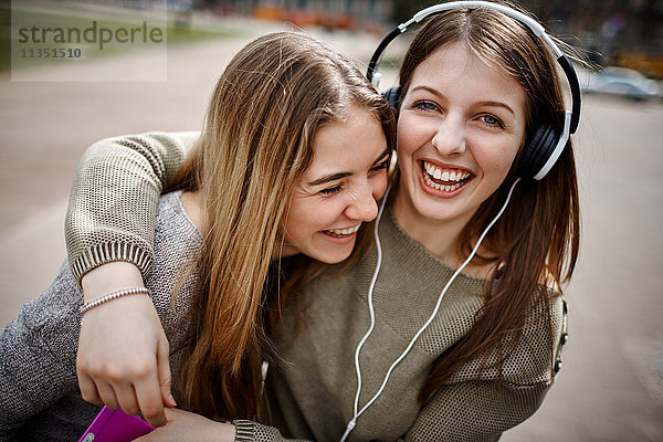 Glückliche junge Frau mit Freundin trägt Kopfhörer