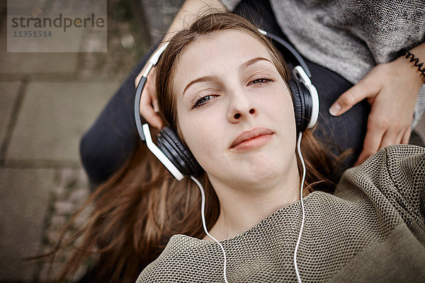 Entspannte junge Frau mit Kopfhörern liegt auf dem Schoß ihrer Freundin