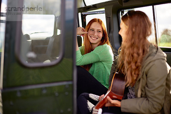 Lächelnde junge Frau schaut auf ihre Freundin mit Gitarre im Auto