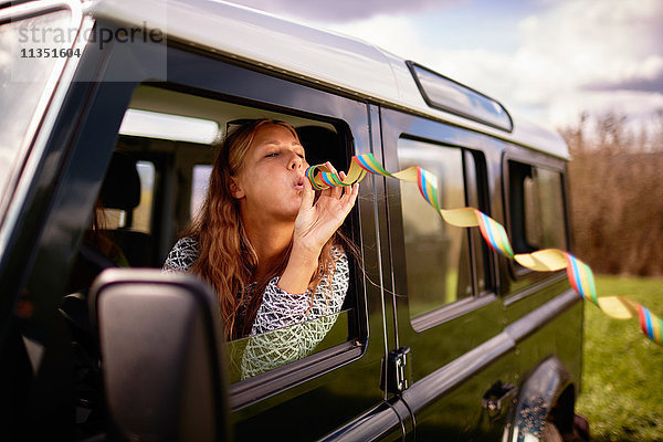 Junge Frau bläst eine Luftschlange aus einem Auto
