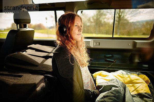 Junge Frau mit Schlafsack und Kopfhörern in einem Geländewagen