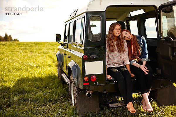 Zwei junge Frauen sitzen im Kofferraum eines Geländewagens auf einer Wiese