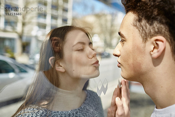 Teenagerpaar küsst sich durch eine Glasscheibe hindurch