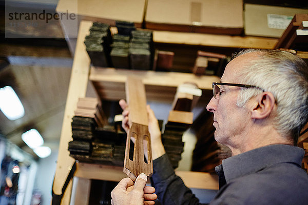 Gitarrenbauer untersucht ein Griffbrett in seiner Werkstatt