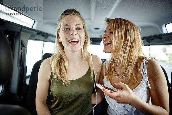Zwei fröhliche junge Frauen im Auto hören Musik und singen