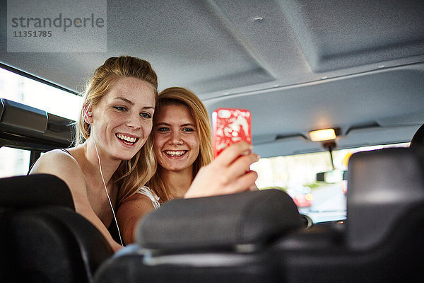 Zwei fröhliche junge Frauen im Auto machen ein Selfie