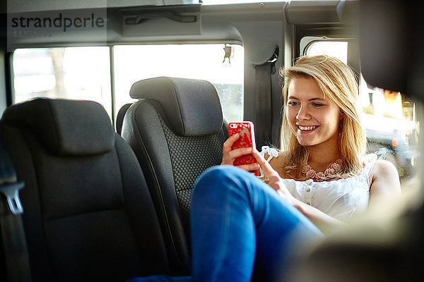 Lächelnde junge Frau im Auto schaut auf ihr Handy