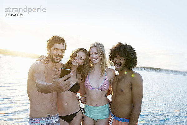 Junge erwachsene Freunde in Bikinis und Badehosen  die sich bei Sonnenuntergang im Sommer selbst tragen.