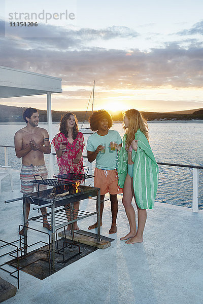 Junge erwachsene Freunde beim Grillen  Abhängen und Trinken auf dem Sommerhausboot bei Sonnenuntergang