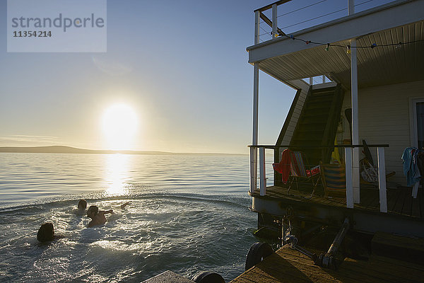 Junge erwachsene Freunde beim Schwimmen in der Nähe des Sommerhausbootes auf dem Sonnenuntergang Ozean