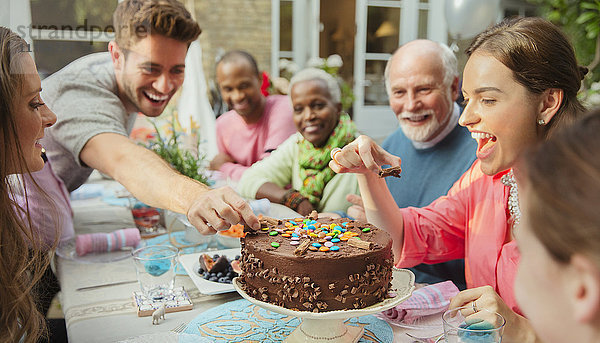 Familie greift nach Bonbons auf Schokoladen-Geburtstagskuchen am Terrassentisch