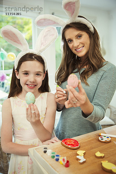 Portrait lächelnde Mutter und Tochter im Kostüm Kaninchenohren mit verzierten Ostereiern
