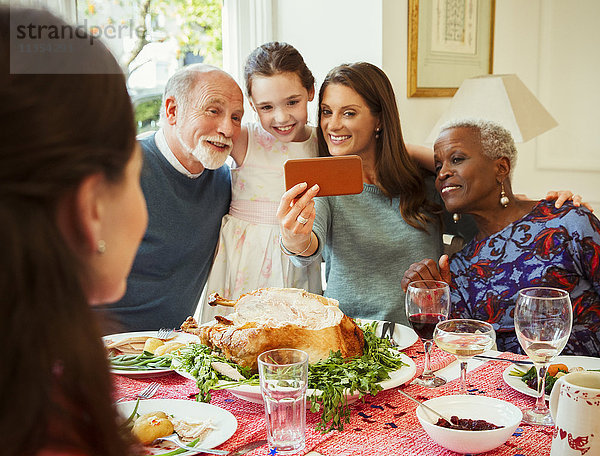 Multi-ethnische Mehrgenerationen-Familie mit Fotohandy  die Selfie am Weihnachtstisch mitnimmt.