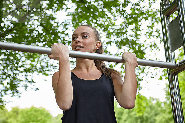 Junge Frau  die im Park trainiert und Klimmzüge an Übungsstangen macht